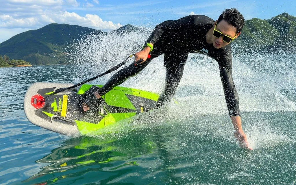 Rider en combinaison sur un E-surf, penché dans un virage, la main dans l'eau