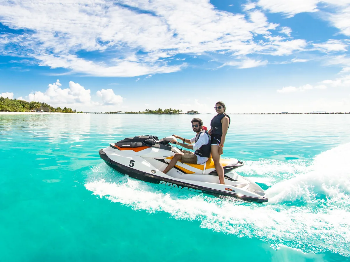 Deux passagers en jet ski sur une eau turquoise, le long d'une plage bordée de cocotiers