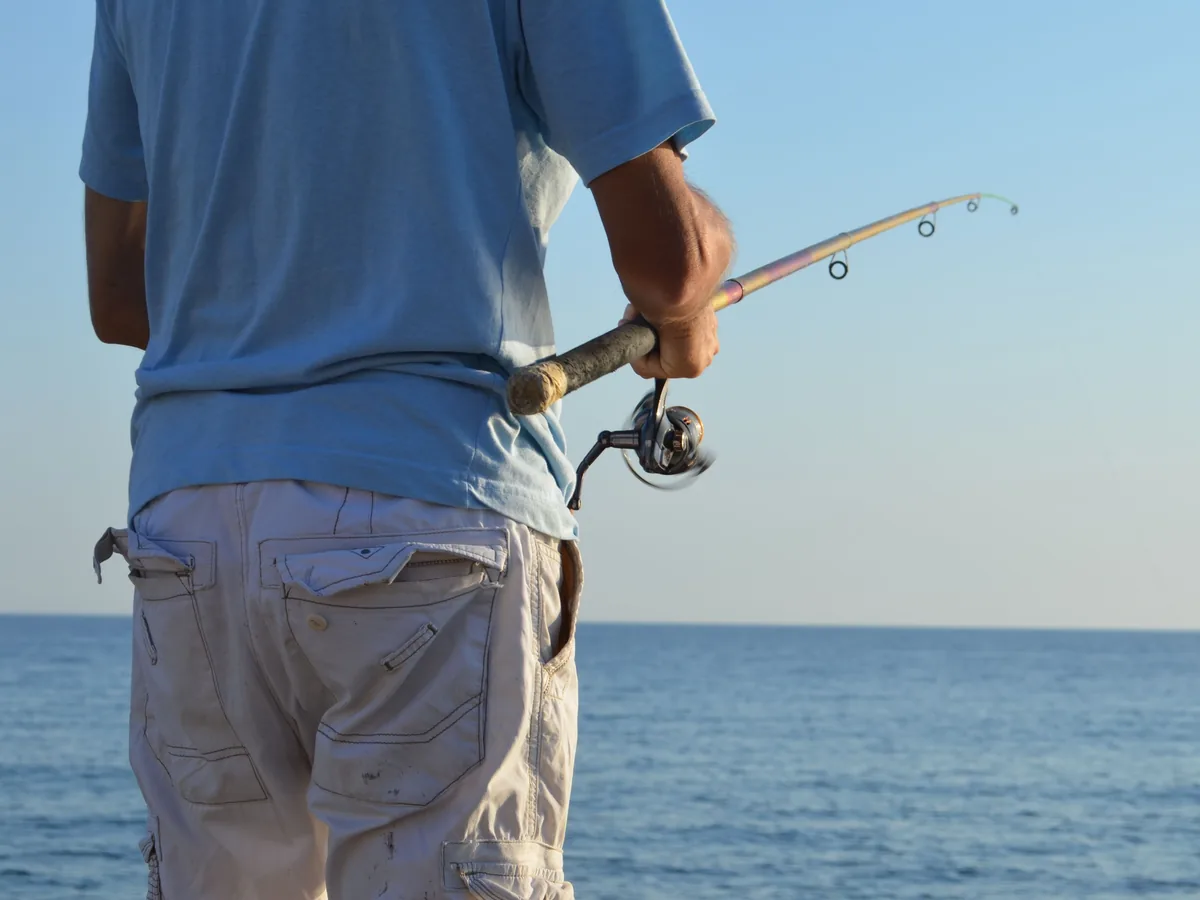 Pêcheur de dos, canne à la main, face à la mer