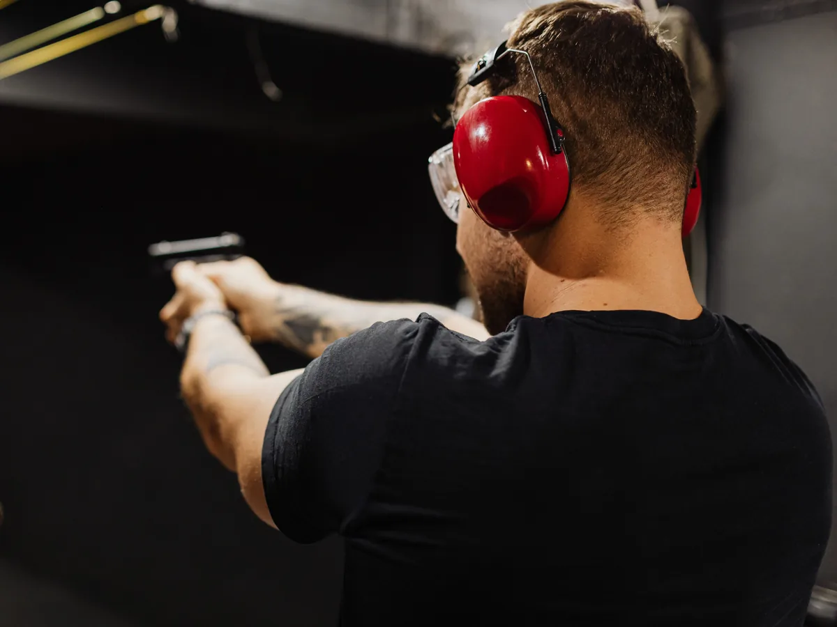 Tireur de dos au stand, casque antibruit et lunettes de protection, pistolet en main