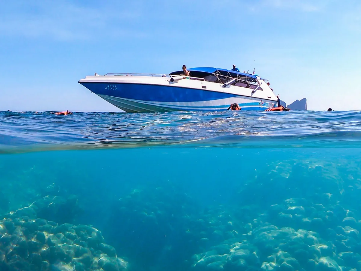 Vue mi-air mi-eau : un bateau en surface, les coraux visibles juste en dessous